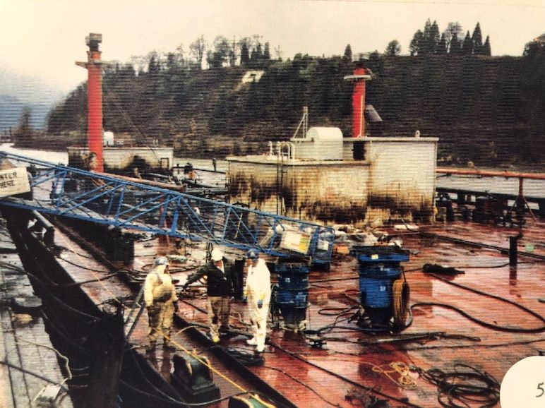 Photo of the deck of the Nestucca in port. Three crew members in hard hats are talking mid-deck