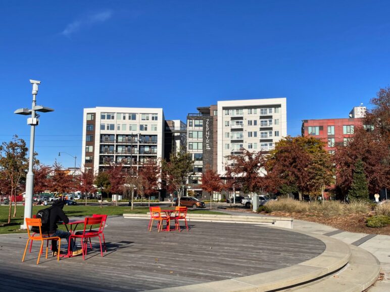 Recently constructed apartments near Redmond’s future Link light rail station, ranging from six to eight stories. Sunny day at Redmond's park with apartments in the background. A person is in the foreground of the park on a boardwalk
