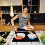 Photo of person cooking on an induction stove, using tongs to lift food onto a plate