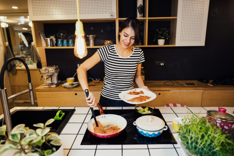 Photo of person cooking on an induction stove, using tongs to lift food onto a plate