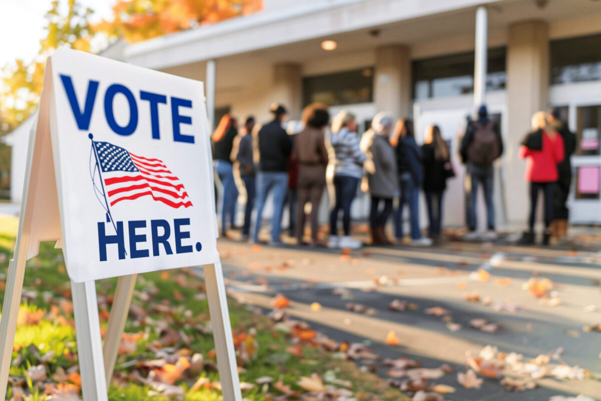 Voters in line outside polling place with Vote Here sign in foreground